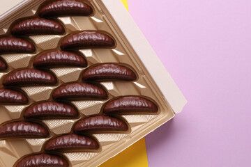 Box of chocolate candies on yellow purple background. Top view