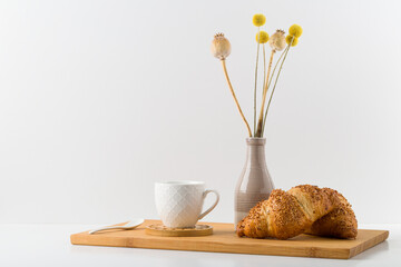 Plate with croissant and vase with flower standing on wooden table in the kitchen. Healthy light meals for breakfast.