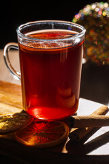 Glass cup of warm red beverage with dried citrus slices and cinnamon sticks on a wooden board