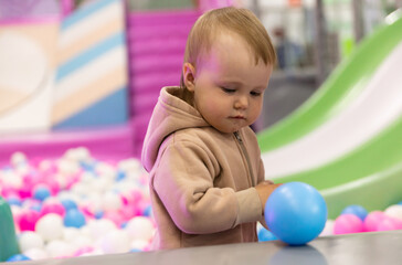 Fototapeta premium Cute little baby plays with balls in a dry pool at a children's entertainment center