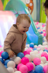 Cute little baby plays with balls in a dry pool at a children's entertainment center