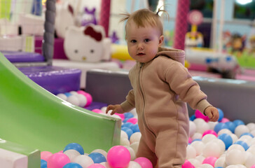 Cute little baby plays with balls in a dry pool at a children's entertainment center