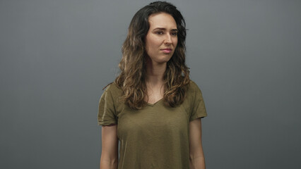 Woman in olive t shirt tilts head while furrowing brow and wrinkling nose in grey studio; skepticism.