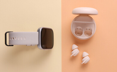 Modern Wireless Bluetooth Earbuds with Charging Case and smart watch on Beige Background. Top view. Flat lay
