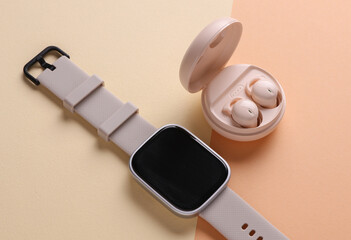 Modern Wireless Bluetooth Earbuds with Charging Case and smart watch on Beige Background. Top view. Flat lay