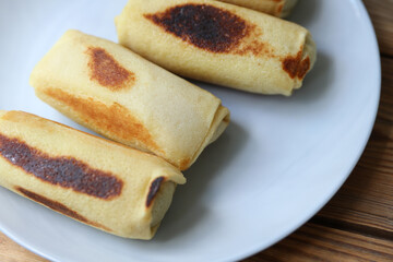 Roll pancakes with filling on plate, Wooden background