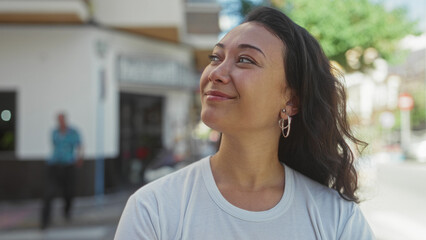 Young hispanic woman smiling with face turned upward on a sunlit city street; contentment reflection.