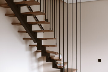 Modern floating staircase with wooden steps and black metal railings. A stack of books rests on the steps of this contemporary staircase, adding a touch of warmth to the minimalist design. Home space.