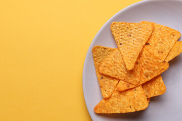 Triangular appetizing corn tortilla chips slices in plate on yellow background