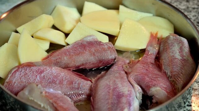 The raw redfish (red mullet) and potatoes in a baking pan