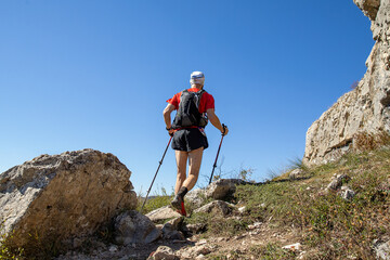 Man with trekking poles and backpack climb mountain trail