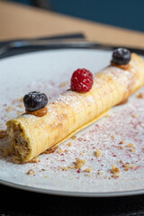 Rolled pancake topped with fresh raspberries and blueberries sprinkled with powdered sugar on a white plate