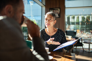 Senior woman consulting with adult colleague at cafe, engaged