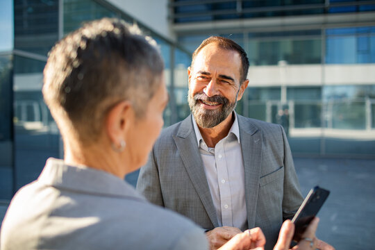 Mature business colleagues smiling during conversation outside office building - Powered by Adobe