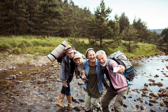 Senior friends taking a joyful selfie while hiking by a forest river