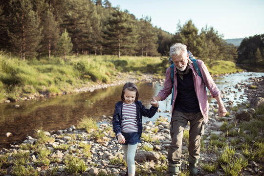 Senior grandfather and child granddaughter hiking happily by a forest river