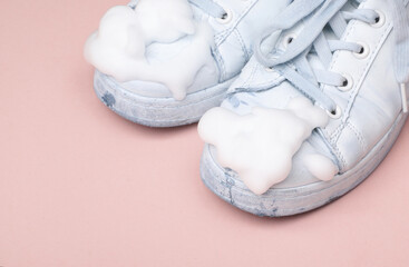 Old White sneakers with cleaning foam  on pink background. Shoe care