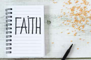 Faith, handwritten text in notebook with mustard seeds on wooden background. Top view. Christian...
