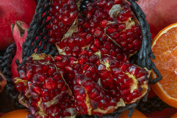 Open pomegranate with red seeds surrounded by whole fruits and orange slice. Pomegranates in rustic basket showcasing vibrant colors juicy textures and organic produce for culinary.