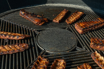 Grilled ribs cooking on round barbecue grill. Delicious barbecue pork ribs with crispy dry rub seasoning placed on circular grill ready for serving.