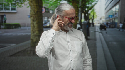 Man pressing hands to ears on a busy street near a tree and storefronts; distress noise sensitivity.