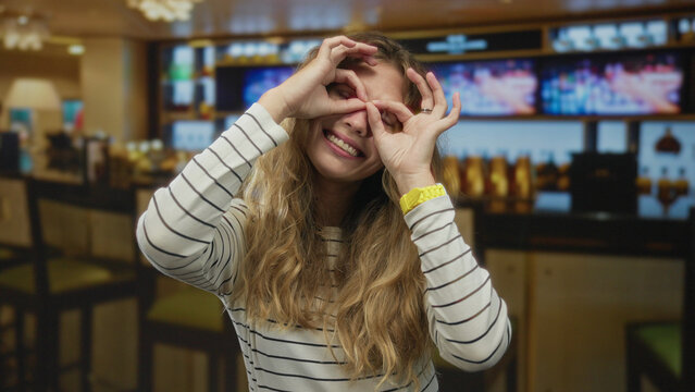Woman holds her hands while smiling inside a cafe where a blonde young guest makes a playful binocular gesture looking very happy. - Powered by Adobe