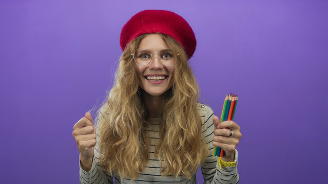 Woman clutches pencils while celebrating in studio, feeling young, blonde, excited and smiling with colorful glasses.