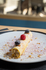 Rolled dessert topped with raspberry and blueberries on a white plate dusted with powdered sugar
