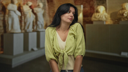 Woman shrugs shoulders before a statue display in museum building under soft gallery lighting;...