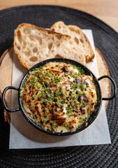 Delicious gourmet cheesy casserole topped with fresh chives served in a black dish with crusty bread