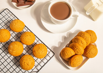 Freshly baked gingerbread cookies cooling on a rack, served with a cup of hot tea, chocolate pieces, and milk in a cozy, bright setting.