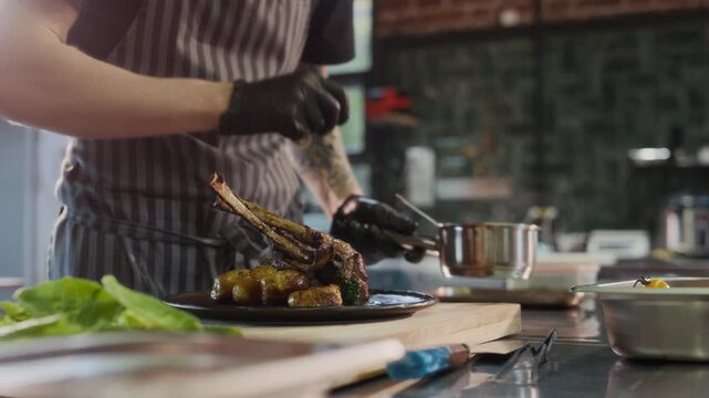 Cinematic close up shot of unrecognizable chef adding sauce to lamb rack dish while preparing for serving in restaurant, copy space