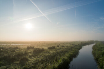 A river with a field of grass and flowers on the banks. The water is calm and the sky is clear in Polder Arkemheen in the Netherlands