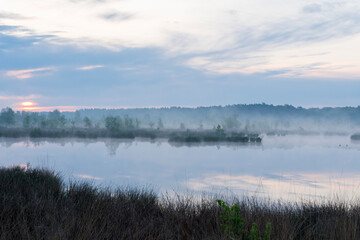In the early morning a lake with a reflection of the sky. The sky is overcast and the air is cool and damp. The scene is quiet and peaceful, with the lake providing a sense of solitude and calm. Dwing