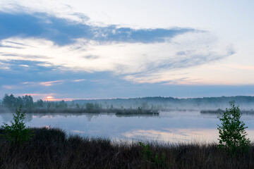 In the early morning a lake with a reflection of the sky. The sky is overcast and the air is cool and damp. The scene is quiet and peaceful, with the lake providing a sense of solitude and calm. Dwing