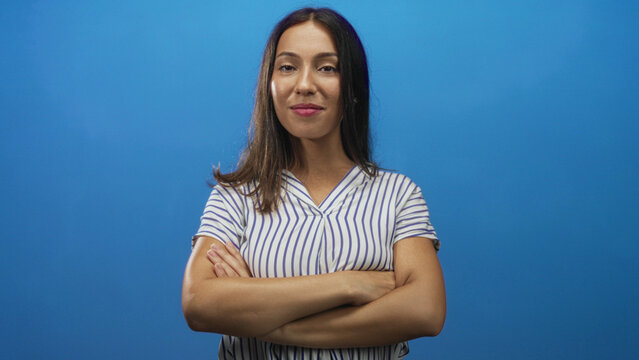Woman with arms crossed showing bare forearms and folded hands in studio against bright blue backdrop; confidence empowerment.