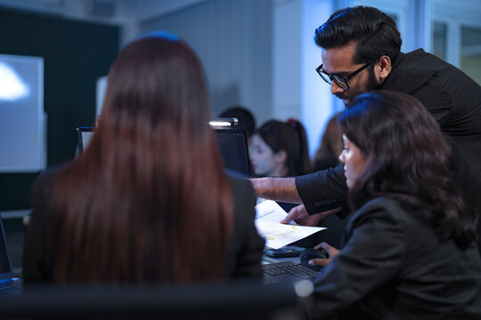 A human supervisor trains a new employee on how to collaborate with their AI partner, guiding her on prompt engineering and interpreting the AI's complex data analysis for decision-making.