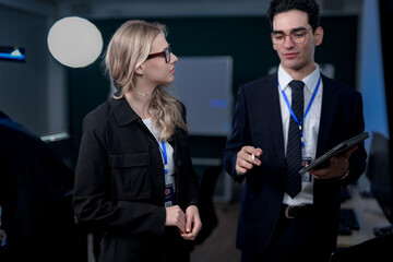 A male team leader in a suit uses a stylus to explain a complex project on a large screen, providing one-on-one training to a female colleague in a modern, high-tech office.