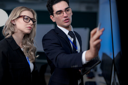A senior software developer leads a code review session, pointing to a specific function on the screen to explain its logic and syntax to a junior engineer before a major deployment.