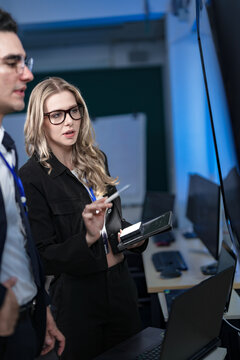 A senior software developer leads a code review session, pointing to a specific function on the screen to explain its logic and syntax to a junior engineer before a major deployment.
