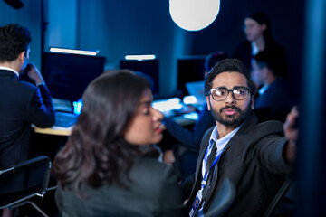 A creative director leads a late-night review session, pointing out key design elements on a large screen to his team, providing artistic direction for a new marketing campaign or UI project.