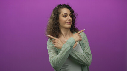 Woman pointing finger to the left in a purple studio wall while looking up and smiling; curiosity guidance.