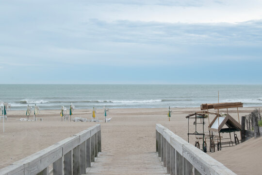 Wooden walkway leading to an empty beach with closed umbrellas and calm waves.