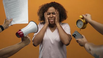 Woman holding head with hands while surrounded by megaphone, papers, alarm clock and smartphone in...
