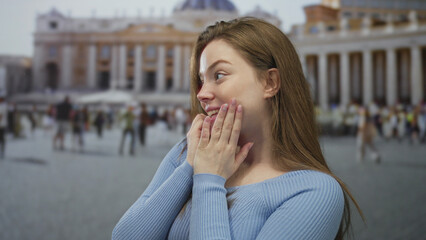 Woman in blue sweater holds hands to cheeks in an outdoor building square near monumental colonnade...