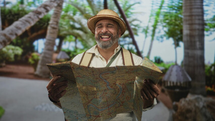 Man holding map and smiling while reading in park wearing pith helmet and backpack; adventure discovery.