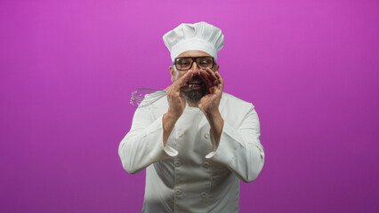 Man chef, middle aged with grey hair and beard, wearing white chef uniform and hat, holding a whisk and cupping hands to shout in a magenta studio backdrop; confidence.