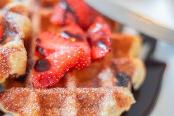 Appetizing sliced ​​strawberries on a freshly baked waffle, topped with chocolate sauce