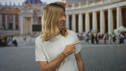 Blond man points finger to the right at ornate building colonnade in building setting with crowd...
