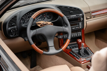 1990s car interior with wooden accents. Steering wheel and dashboard of an old open-top vehicle. Leather gloves on top of steering column.